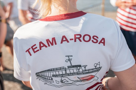 Rückansicht eines weißen T-Shirts mit rotem Kragen und Aufdruck TEAM A-ROSA sowie einer Schiffsgrafik.
