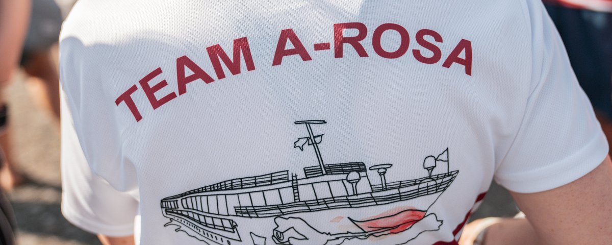 Rückansicht eines weißen T-Shirts mit rotem Kragen und Aufdruck TEAM A-ROSA sowie einer Schiffsgrafik.