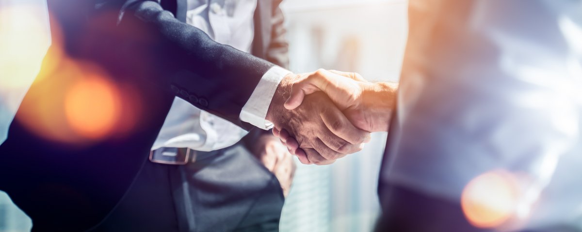Zwei Personen schütteln sich die Hände in einem hellen Büro mit Sonnenlicht