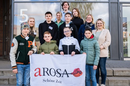 Gruppenfoto von Jugendlichen und Erwachsenen vor einem Gebäude, vorne halten vier Jungen ein Banner mit dem Schriftzug A-ROSA Schöne Zeit.