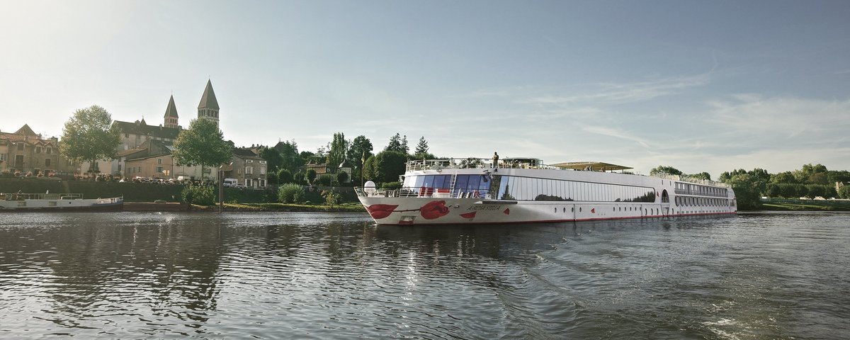Die A-ROSA STELLA fährt auf einem ruhigen Fluss vor einer Stadt mit historischen Gebäuden und zwei Kirchtürmen bei klarem Himmel.