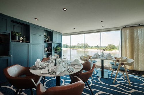 Stilvoll eingedeckter Restaurantbereich der A-ROSA SENA mit bodentiefen Fenstern und Blick auf einen ruhigen Fluss.